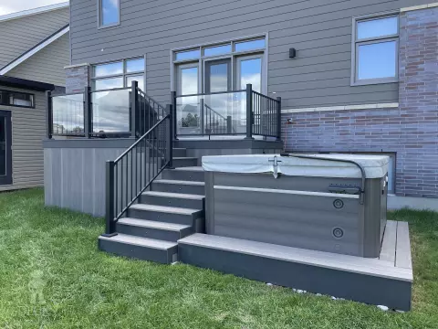 Grey composite deck with glass railings and hot tub access.