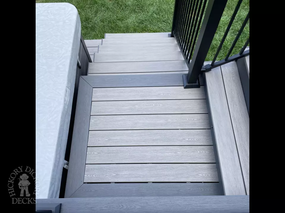 Grey composite deck with glass railings and hot tub access.
