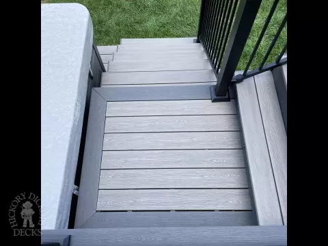 Grey composite deck with glass railings and hot tub access.