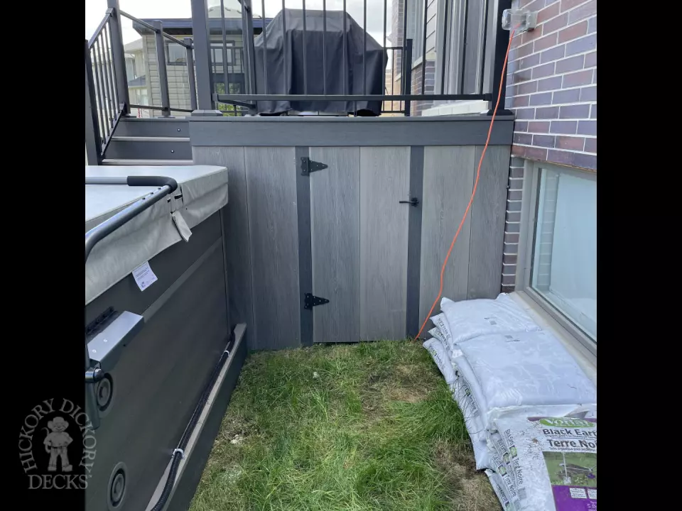 Grey composite deck with glass railings and hot tub access.