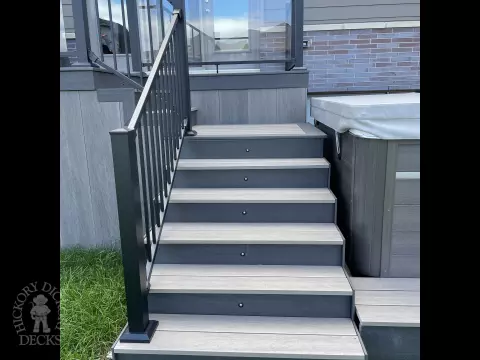 Grey composite deck with glass railings and hot tub access.