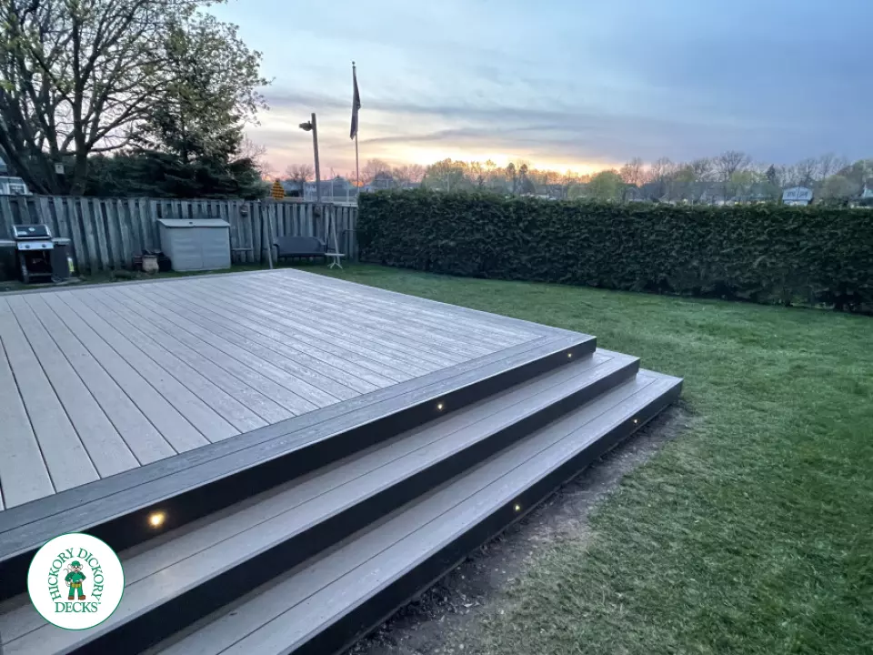 Grey clubhouse deck with wrap around stairs, lighting in steps, and a dark grey border.