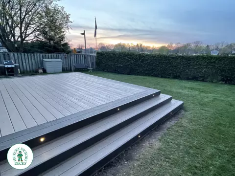 Grey clubhouse deck with wrap around stairs, lighting in steps, and a dark grey border.