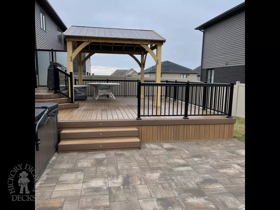 Brown composite deck with a roof structure, glass railings, access to the hot tub, and frosted glass privacy screens.