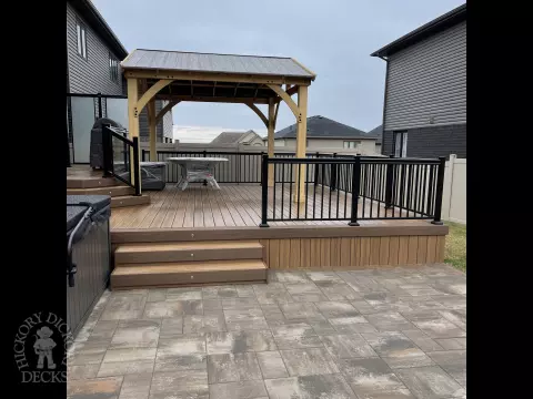 Brown composite deck with a roof structure, glass railings, access to the hot tub, and frosted glass privacy screens.