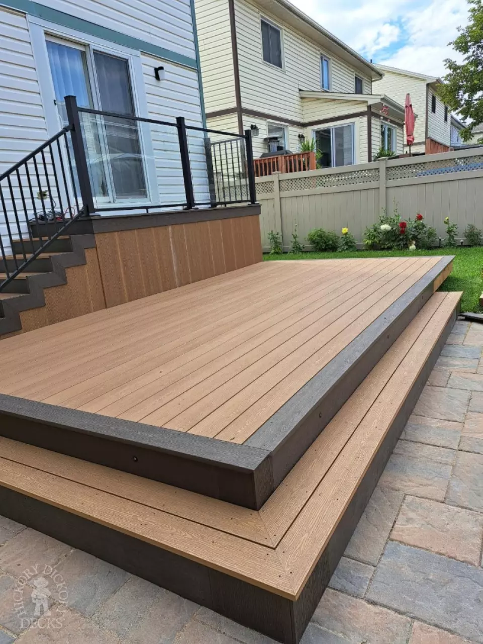 Multi level brown deck with glass railing, and a dark brown border.