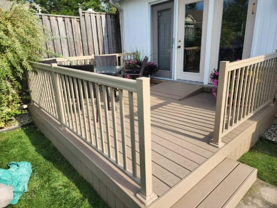Small beige composite deck with beige railings, accessibility ramp into house.