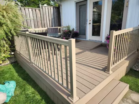Small beige composite deck with beige railings, accessibility ramp into house.
