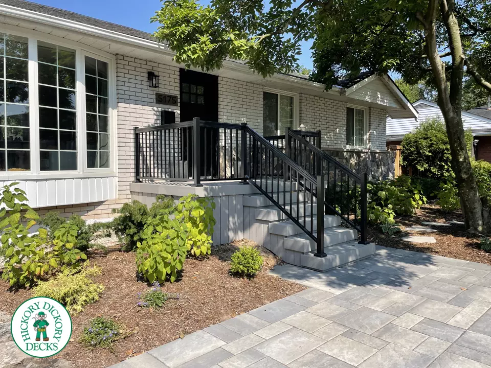 Small grey front porch with steps and black aluminum railing.