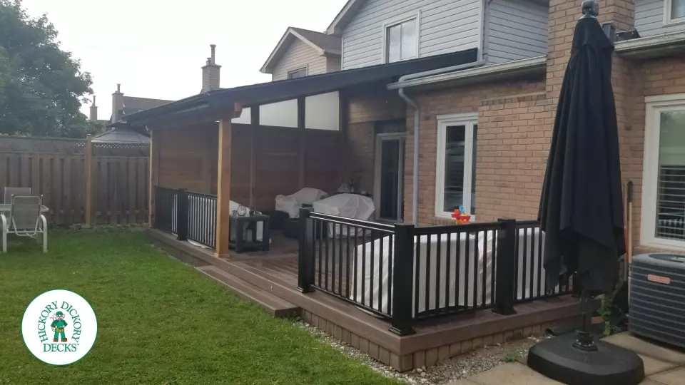 Low brown Veka deck with custom roof structure, black aluminum railing, and lights in steps.