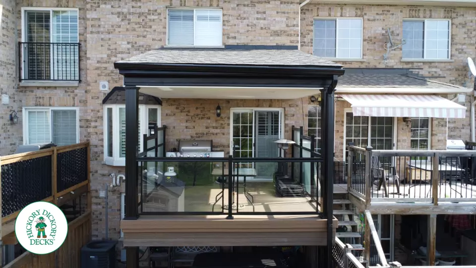 High brown Trex deck with glass railing and a roof structure, with a low deck in the same color and material below.