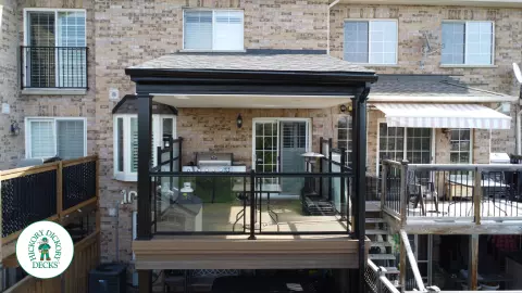 High brown Trex deck with glass railing and a roof structure, with a low deck in the same color and material below.