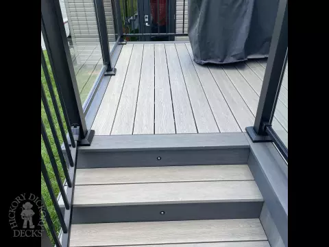 Grey composite deck with glass railings and hot tub access.