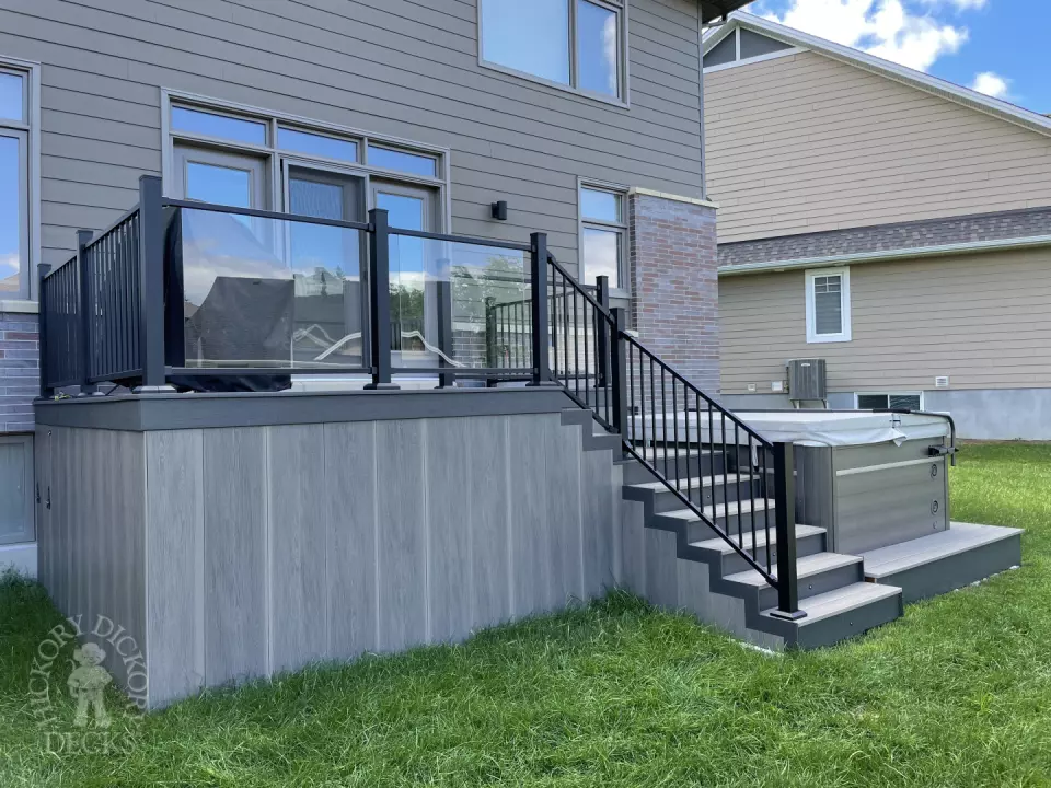 Grey composite deck with glass railings and hot tub access.