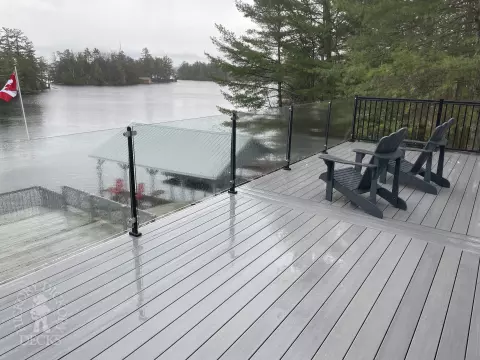 High grey fiberon deck with glass railings looking out to a lake.
