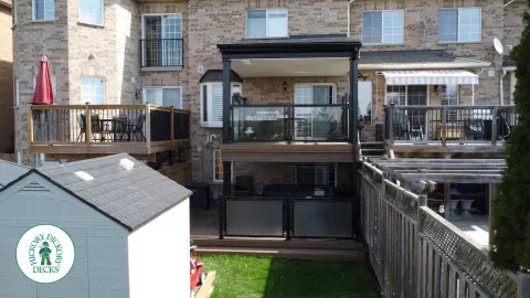 High brown Trex deck with glass railing and a roof structure, with a low deck in the same color and material below.