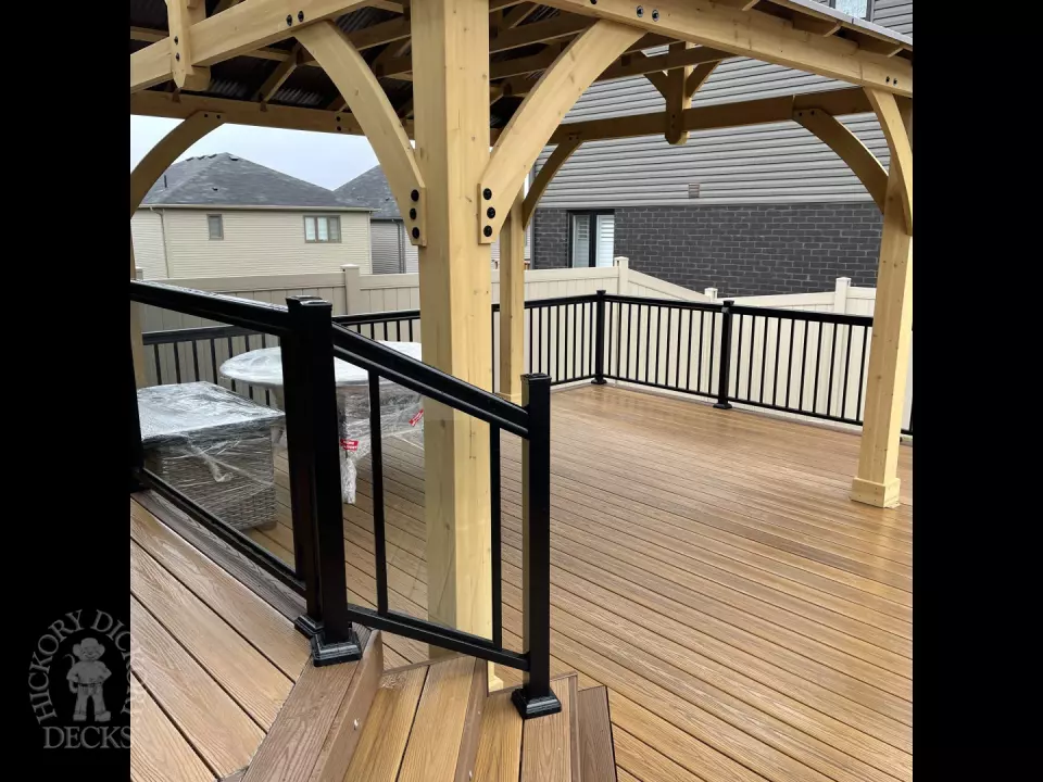 Brown composite deck with a roof structure, glass railings, access to the hot tub, and frosted glass privacy screens.