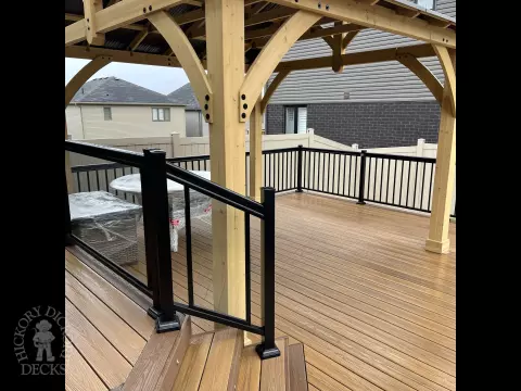 Brown composite deck with a roof structure, glass railings, access to the hot tub, and frosted glass privacy screens.