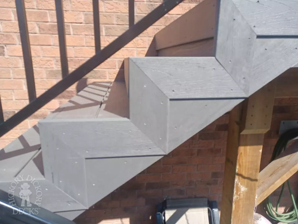 Large multi level grey composite deck with cedar skirt and black aluminum railing.