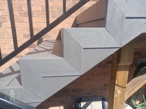 Large multi level grey composite deck with cedar skirt and black aluminum railing.