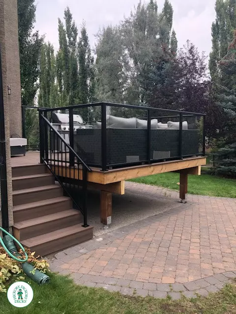 Mid high brown Dekorators deck with steps leading to back yard and glass railings.