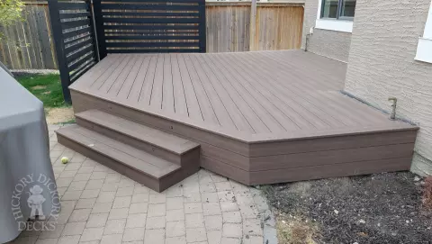 Small brown composite deck with steps and a privacy screen