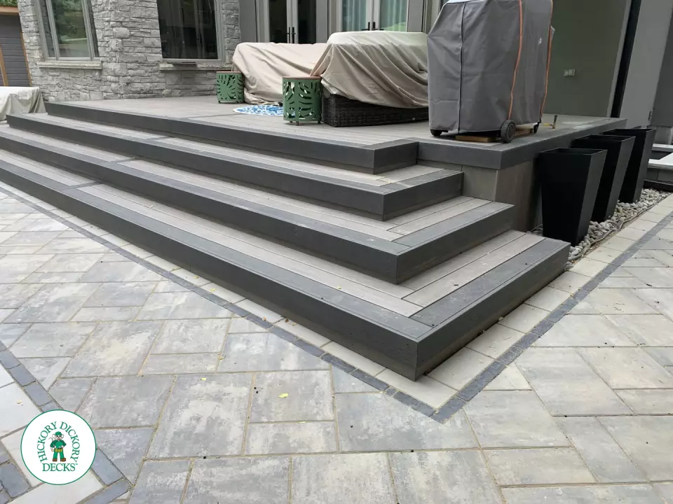 Small dark grey deck with wrap around stairs and glass railings.