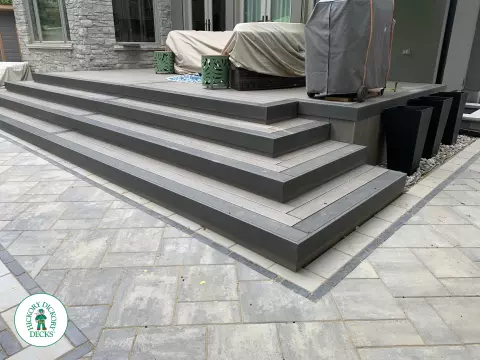 Small dark grey deck with wrap around stairs and glass railings.