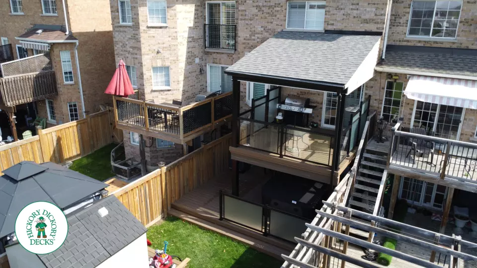 High brown Trex deck with glass railing and a roof structure, with a low deck in the same color and material below.