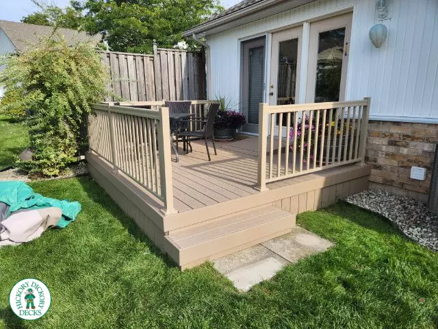 Small beige composite deck with beige railings, accessibility ramp into house.