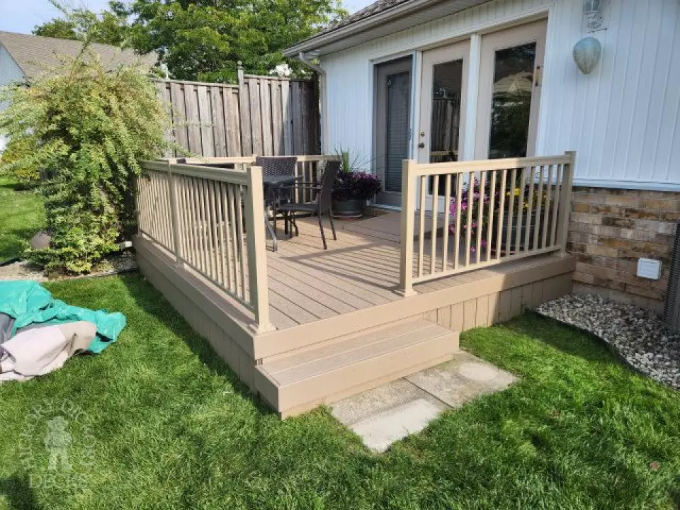 Small beige composite deck with beige railings, accessibility ramp into house.