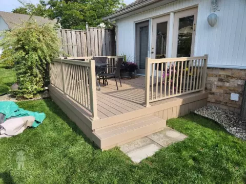 Small beige composite deck with beige railings, accessibility ramp into house.