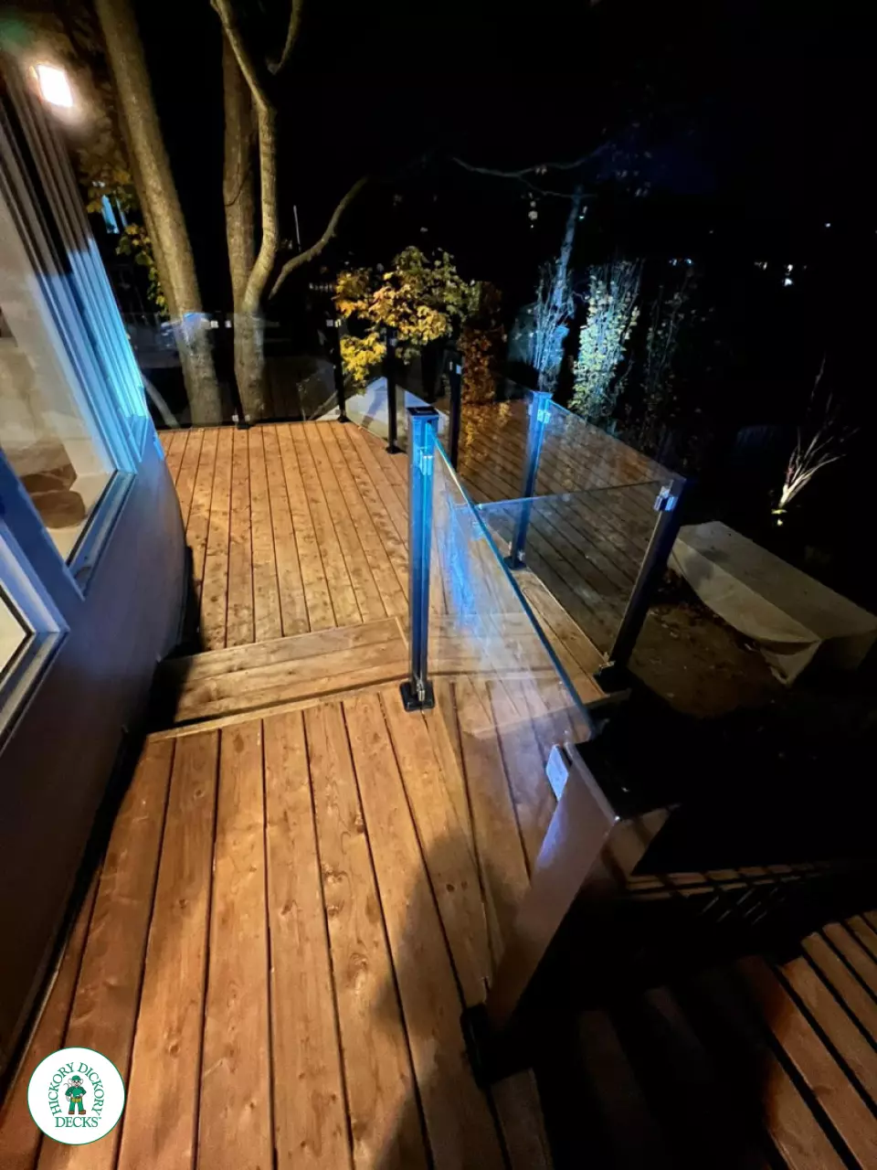 High cedar deck with glass railings and a lighting system around the deck.