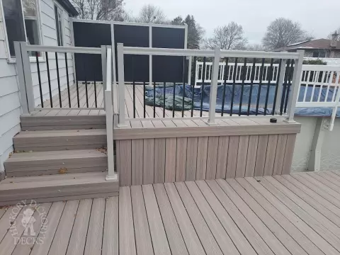 Two level grey Fiberon deck with beige picket aluminum railing and the top level surrounding an above ground pool.