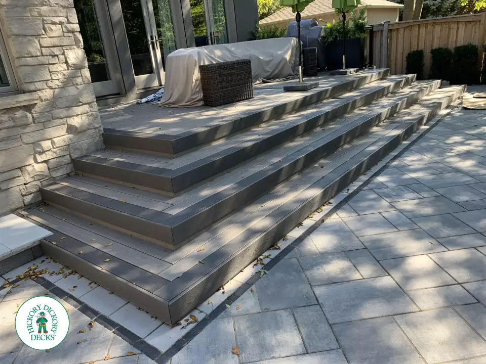 Small dark grey deck with wrap around stairs and glass railings.