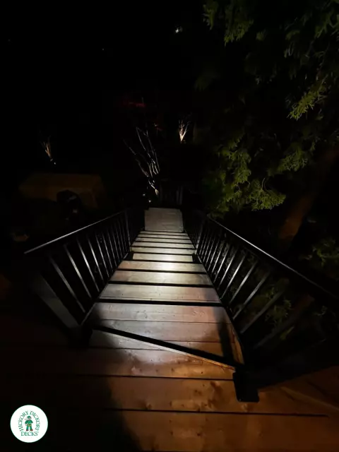 High cedar deck with glass railings and a lighting system around the deck.