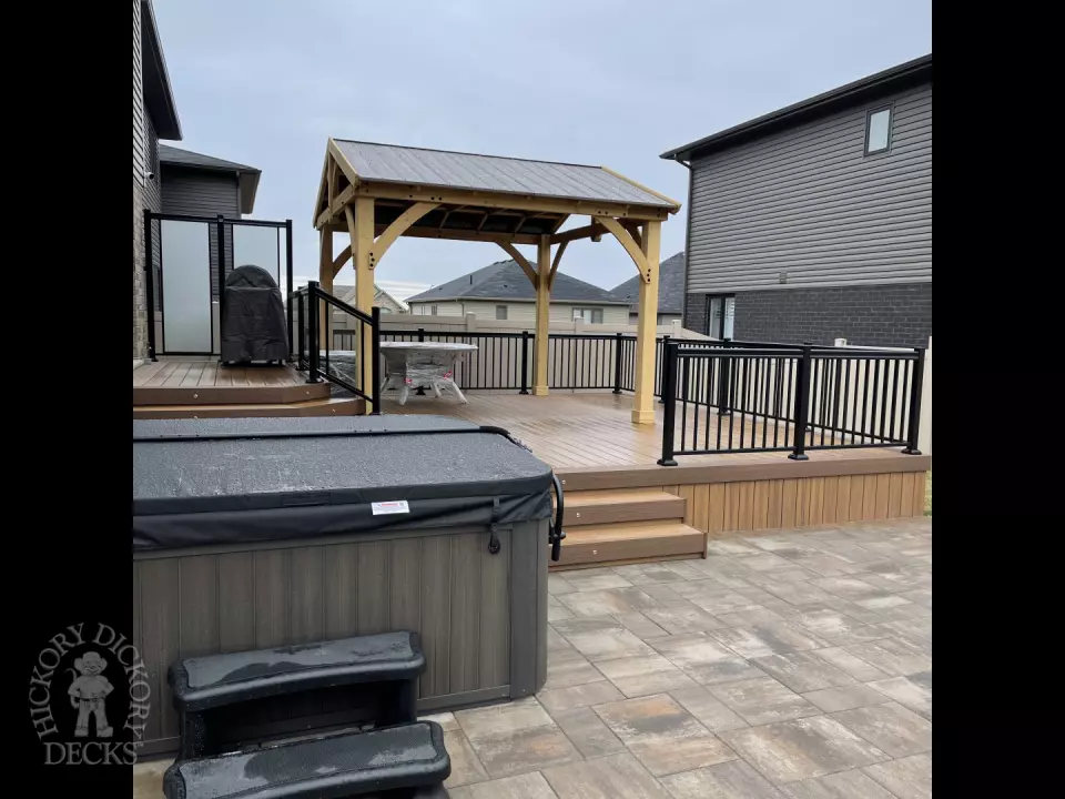 Brown composite deck with a roof structure, glass railings, access to the hot tub, and frosted glass privacy screens.