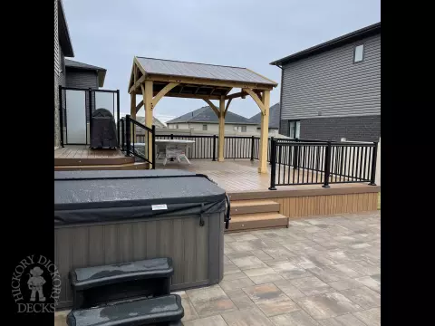 Brown composite deck with a roof structure, glass railings, access to the hot tub, and frosted glass privacy screens.