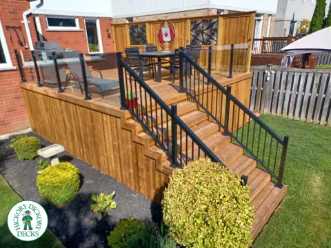 Mid rise pressure treated deck with glass railings, steps, and a custom cedar privacy screen