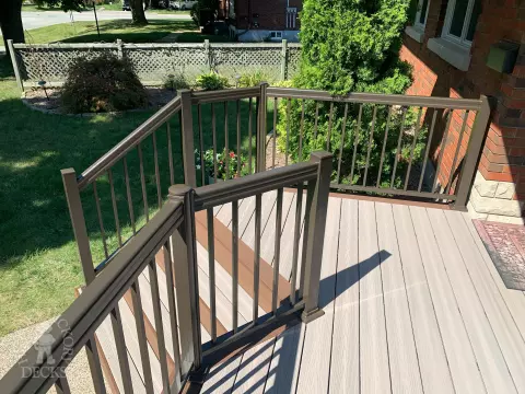 Grey front porch with brown trim and brown aluminum railing.