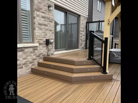 Brown composite deck with a roof structure, glass railings, access to the hot tub, and frosted glass privacy screens.