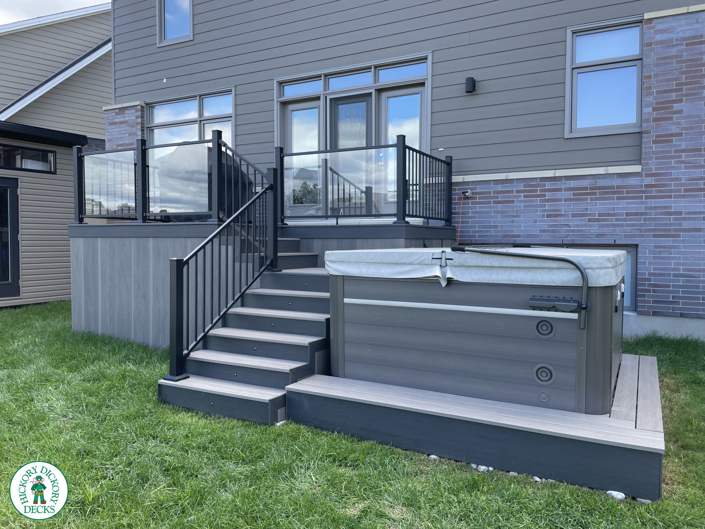 Grey composite deck with glass railings and hot tub access.
