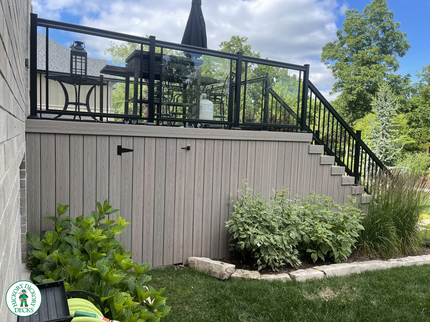 High walk out grey composite deck with aluminum railing on the stairs, and glass style railing around the deck.
