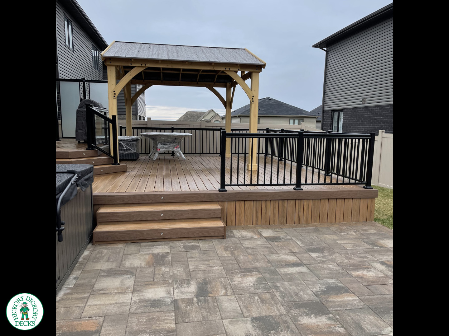 Brown composite deck with a roof structure, glass railings, access to the hot tub, and frosted glass privacy screens.