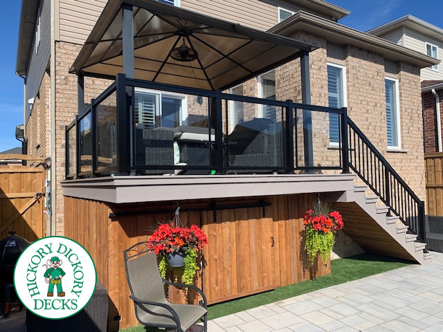 Grey composite deck with aluminum railing and cedar skirt. This deck has glass railings and a shade structure.