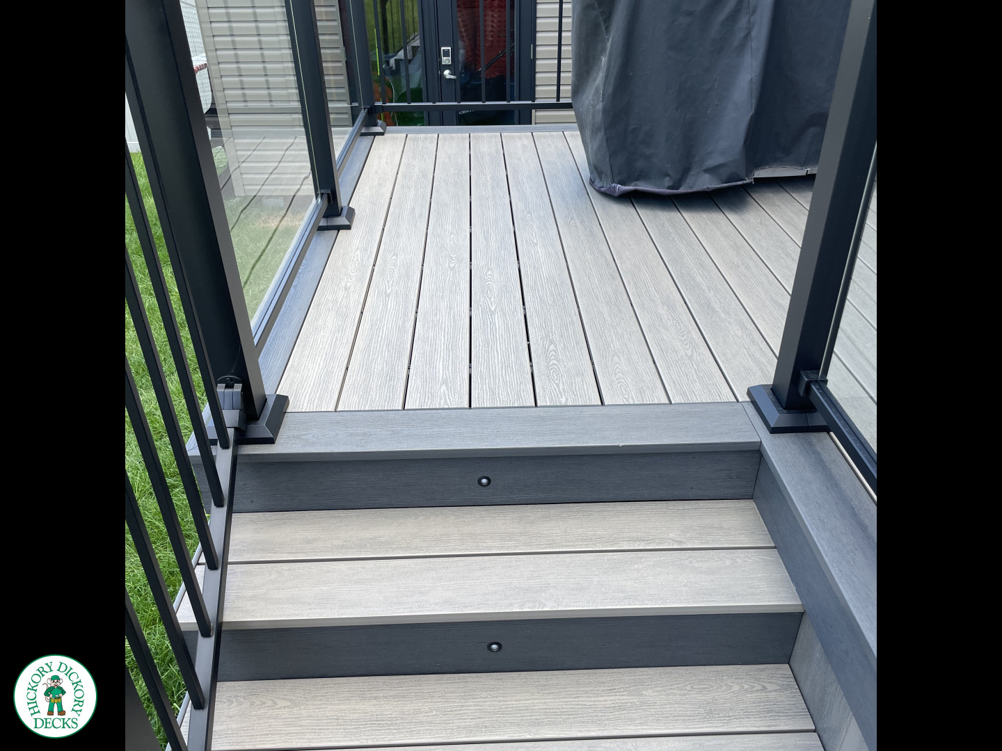 Grey composite deck with glass railings and hot tub access.