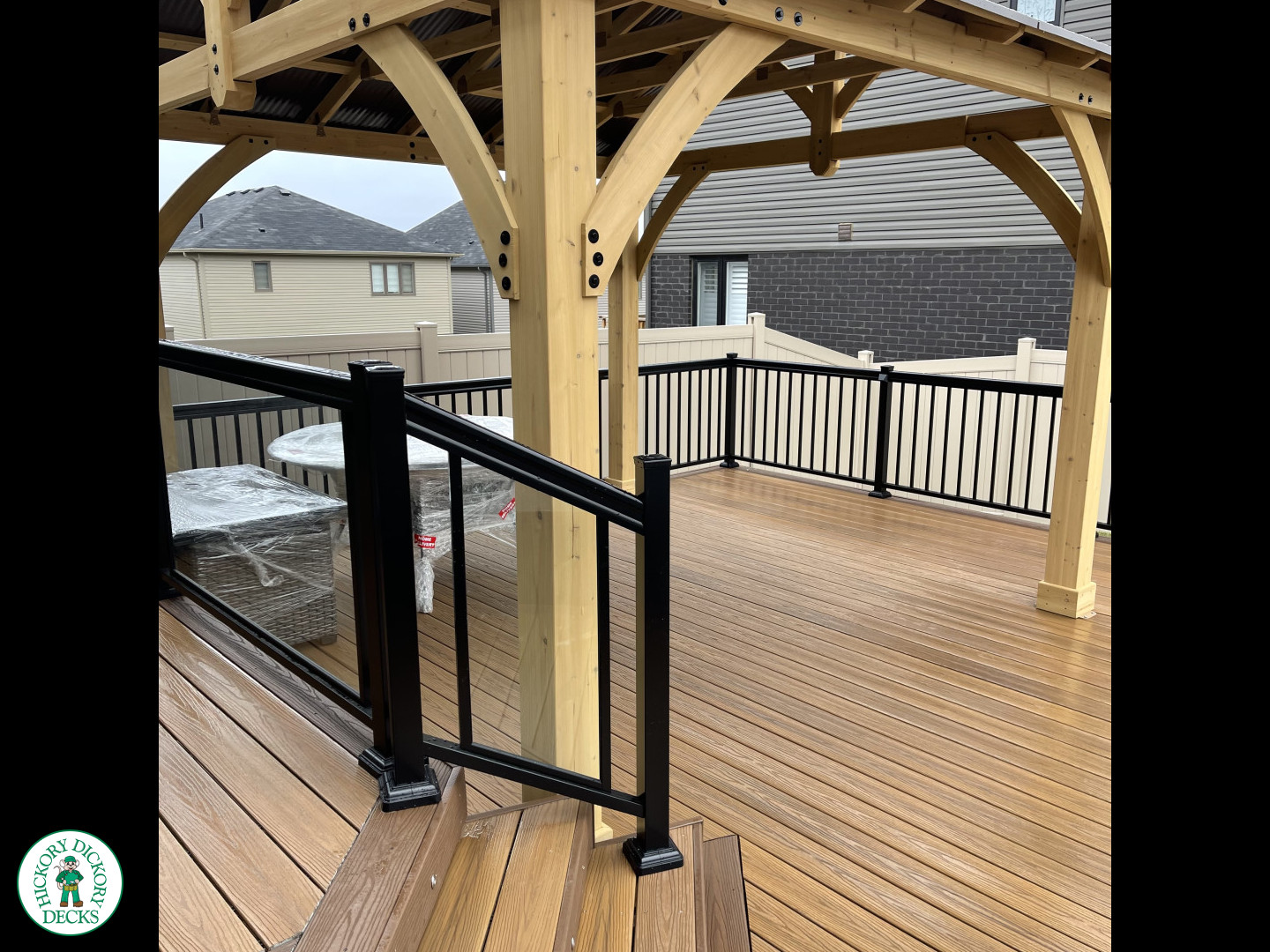 Brown composite deck with a roof structure, glass railings, access to the hot tub, and frosted glass privacy screens.