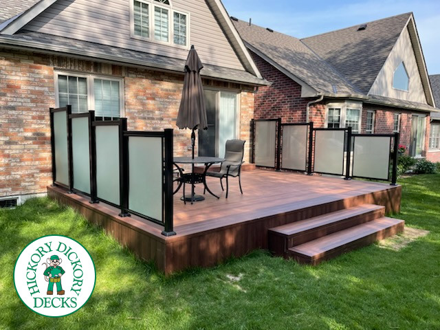Small brown composite deck with frosted glass privacy screen and steps leading to the backyard.