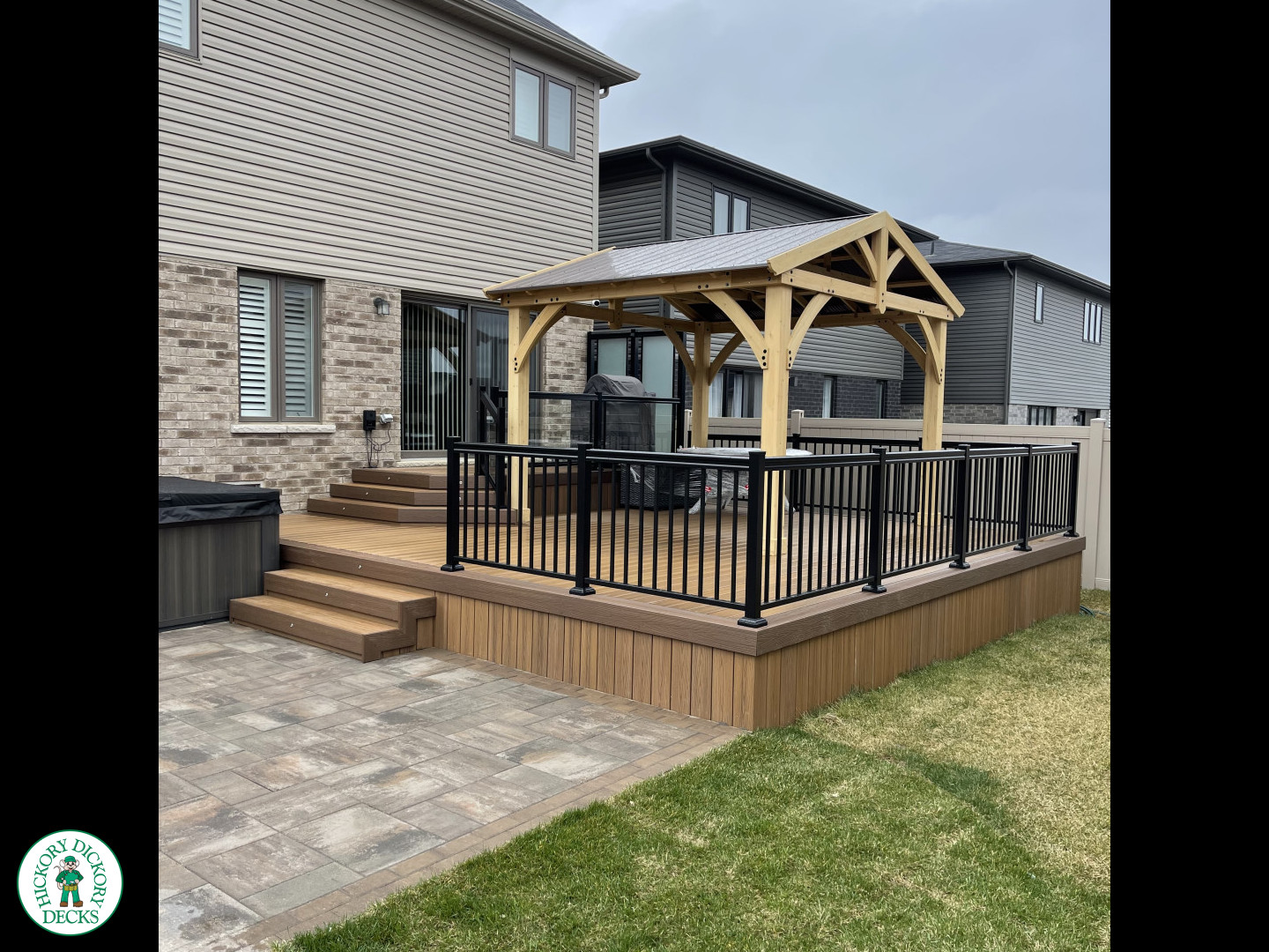 Brown composite deck with a roof structure, glass railings, access to the hot tub, and frosted glass privacy screens.