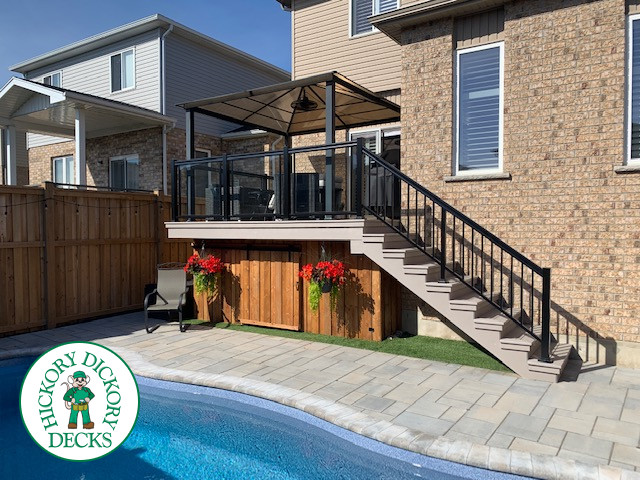 Grey composite deck with aluminum railing and cedar skirt. This deck has glass railings and a shade structure.